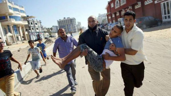 A Palestinian carries a wounded boy following an Israeli military strike (AFP/File Photo)
