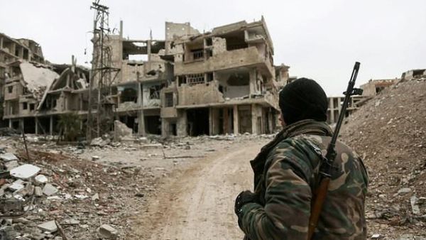 A Syrian opposition fighter from Failaq al-Rahman brigade carrying a sniper rifle walks down a street full of damaged and partially destroyed buildings on the frontline in the rebel-held enclave of Eastern Ghouta near Damascus on February 15, 2018 (AFP) 