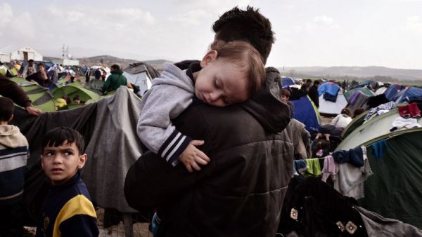 A baby sleeps in the arms of a man in the makeshift refugee and migrant camp at the Greek-Macedonian borders on March 1, 2016, where thousands are stranded due to travel restrictions on migrants. (AFP/Louisa Gouliamaki)