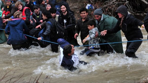 Migrants and refugees cross a river on their way to Macedonia from a makeshift camp at the Greek-Macedonian border on March 14, 2016, where thousands are stranded by the Balkan border blockade. (AFP/Sakis Mitrolidis)