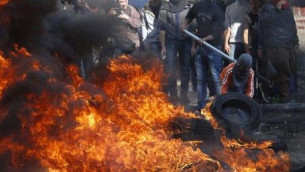 صبي فلسطيني يرتدي قناعا يشعل النار في إطار خلال اشتباكات مع قوات اسرائيلية في الخليل بالضفة الغربية
