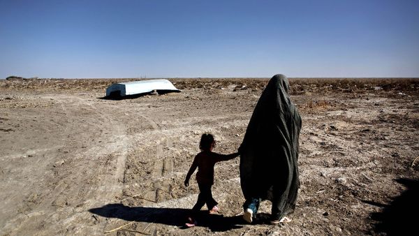 An Iranian woman and her daughter walk past an abandoned boat in the village of Sikh in the Hamoun wetland, where once-flourishing plants and animals have been killed by drought, on Feb. 2, 2015. (AFP/File)