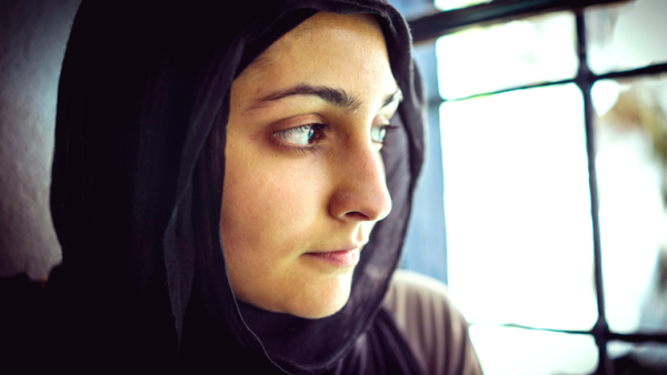 Muslim woman wearing a headscarf looks out a window. (Shutterstock)
