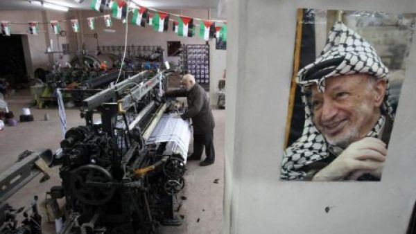 A poster of iconic keffiyeh-wearer Yasser Arafat overlooks as textile machines weave the scarves - symbols of Palestinian pride - at Hebron's Herbawi Textile Factory.  (AFP/Hazem Bader)