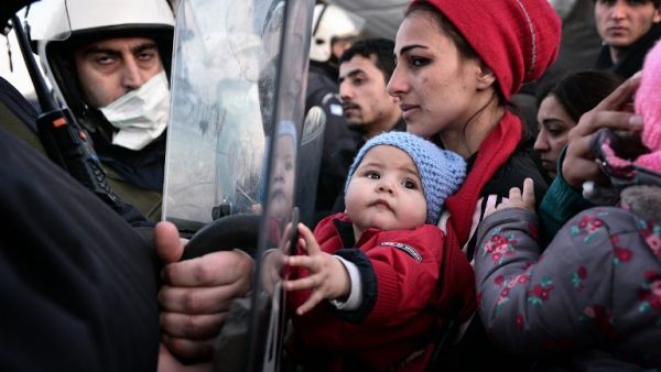 A woman holds a baby as migrants and refugees stand facing Greek police while waiting to cross into Macedonia on March 2, 2016, where thousands of people are stranded. (AFP/Louisa Gouliamaki)