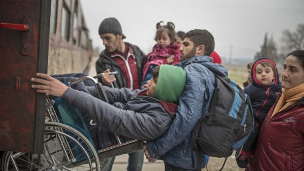 A man helps another young man in a wheelchair as migrants and refugees board a train after crossing the Greek-Macedonian border, near Gevgelija, on February 24, 2016. (AFP/Robert Atanasovski)