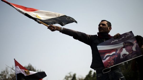 An Egyptian protestor waves his national flag while holding a poster of slain former Egyptian president Anwar Sadat with a slogan reading in Arabic "Man of war and peace" during a demonstration in support of the Egyptian army and against the Muslim Brotherhood. (AFP PHOTO/GIANLUIGI GUERCIA)