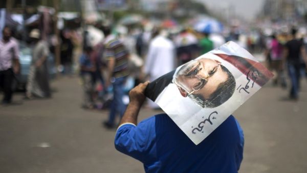 An Egyptian supporter of the Muslim Brotherhood walks holding a poster featuring deposed president Mohamed Morsi during a rally to support him on July 6 (Mahmud Hams / AFP)