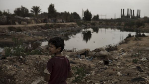 A Bedouin boy stands near an open pool of sewage in the garbage filled Wadi Gaza in the central Gaza Strip on November 27, 2013, as the silhouette of the Gaza Strip power plant is seen in the background. (AFP)