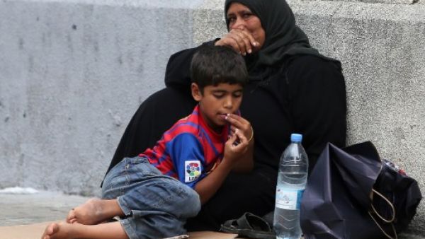 A Syrian refugee boy sits with his mother as they beg on the sidewalk in Beirut (AFP)