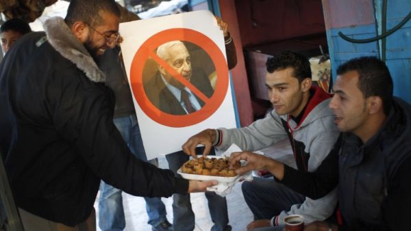 A Palestinian supporter of the Islamic Jihad distributes sweets in a street of the southern Gaza Strip town of Khan Yunis as a boy holds a poster bearing a portrait of former Israeli premier Ariel Sharon. (AFP)

