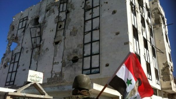 A Syrian army's soldier a national flag featuring Syria's President Bashar Assad in front of a building left in ruins with on Wednesday in Qusayr. AFP Photo