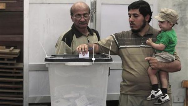 رجل يحمل طفلا ويدلي بصوته في مركز للاقتراع في القاهرة.