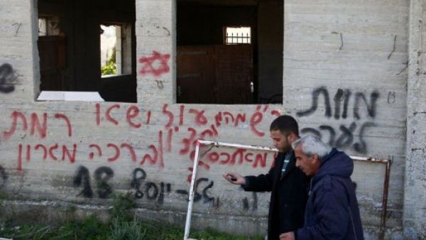 فلسطينيان يمران امام جدار عليه عبارات بالعبرية كتبها مستوطنون بالقرب من رام الله بالضفة الغربية
