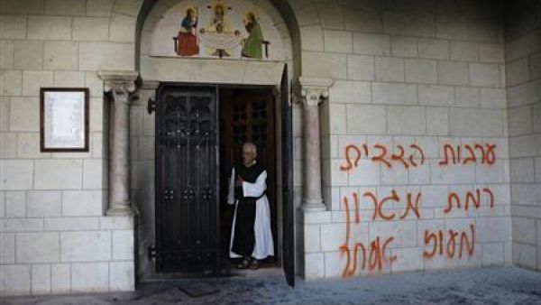 راهب يقف بجوار حائط دير مسيحي شوهه احد الاسرائيليين
