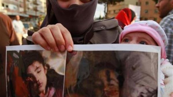 لاجئة سورية تحمل صور اطفال قتلوا في اعمال عنف في سوريا
