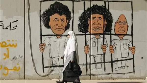 امراة تمر أمام رسم على جدار للزعيم الليبي الراحل معمر القذافي وابنه سيف ورئيس مخابراته عبدالله السنوسي في طرابلس 
