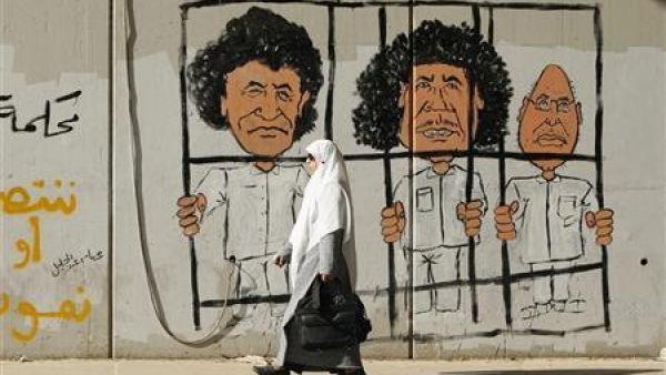 امراة تمر أمام رسم على جدار للزعيم الليبي الراحل معمر القذافي وابنه سيف ورئيس مخابراته عبدالله السنوسي في طرابلس 
