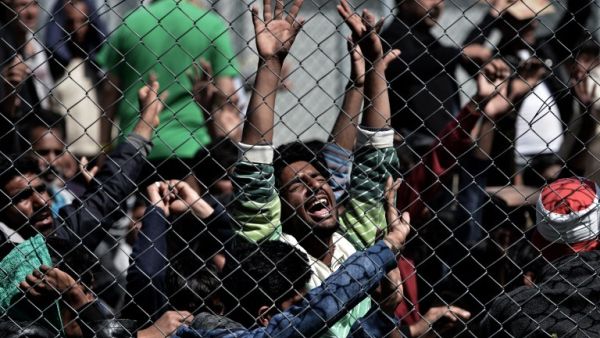 Migrants from Pakistan and Afghanistan stand near a chain-link fence at a detention center in Lesbos. (AFP/Aris Messinis)