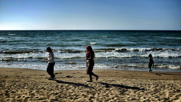 Two women walk along the beach with a child in Myrsini on April 20, 2016, a few metres away from a summer resort sheltering nearly 350 Syrian refugees. (AFP/Aris Messinis)