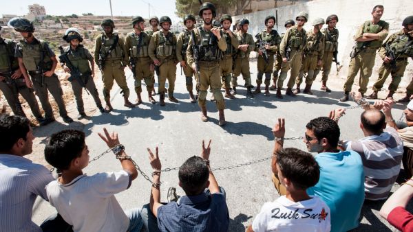 Palestinians in chains symbolizing solidarity with prisoners in Israeli jails face soldiers during a protest in Al Ma'sara, West Bank. (Shutterstock/ File)