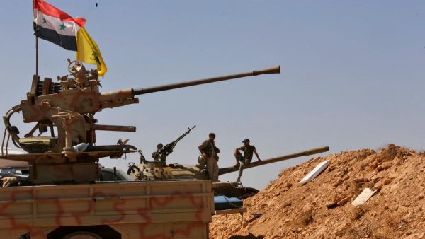 Syrian forces stand on a tank next to vehicles waiting to transport ISIL fighters away from Syria's Qalamoun region on August 28, 2017 as part of a deal brokered by the Iran-backed Lebanese group Hizbollah. Louai Beshara / AFP