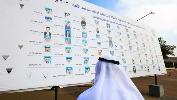كويتي ينظر إلى لافتة انتخابية عليها أسماء المرشحين للانتخابات التشريعية