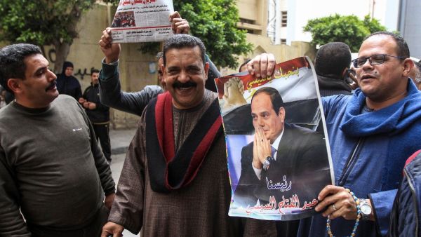 Egyptians pose for a picture with a newspaper front page and a poster of President Abdel Fattah al-Sisi (AFP)