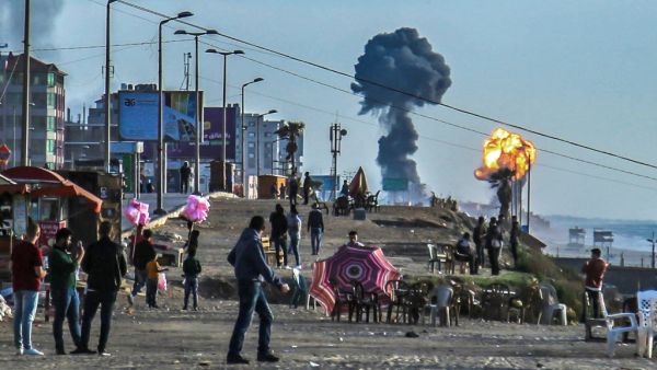 Palestinians gather on the beach in Gaza City as smoke and fire billow following airstrikes by Israel in response to rockets fired by Palestinian militants  (AFP)