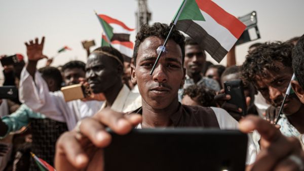 A man poses for a "selfie" photo with a cell phone while having a miniature Sudanese flag placed on his forehead with a plastic suction cap as he awaits the arrival of the deputy head of Sudan's ruling Transitional Military Council (TMC) and commander of the Rapid Support Forces (RSF) paramilitaries, during a rally in the village of Abraq, about 60 kilometers northwest of Khartoum, on June 22, 2019.  Yasuyoshi CHIBA / AFP