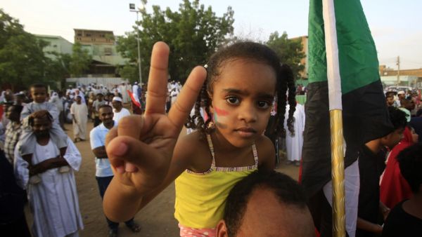 A Sudanese girl wearing facepaint on her cheeks depicting the national flag flashes the victory gesture while seated on the shoulders of a man as people celebrate after protest leaders struck a deal with the ruling generals on a new governing body, in the capital Khartoum's eastern district of Burri  (AFP)