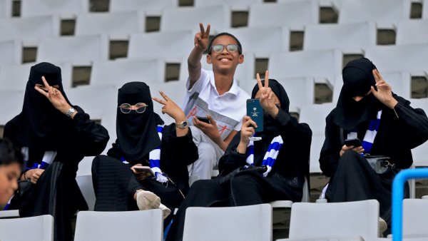 مشجعو كرة القدم السعوديون ، بمن فيهم النساء ، يبثون لفتة النصر وهم ينتظرون فريقهم في المدرجات قبيل مباراة كرة القدم الفاصلة في دوري أبطال آسيا بين الأهلي السعودي والهلال على ملعب جامعة الملك سعود بالعاصمة السعودية الرياض في 13 أغسطس 2019.
