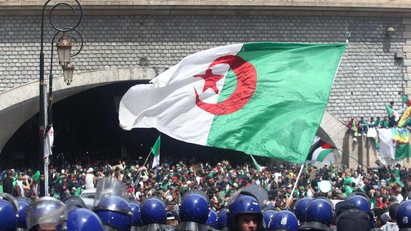 Algerian protesters wave a national flag as security forces stand guard during an an anti-government demonstration in Algiers on April 12, 2019. AFP