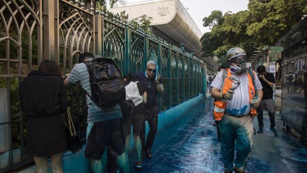 People react after being sprayed with blue-dyed water by a police riot-control vehicle during a protest outside the Kowloon Mosque in Hong Kong
