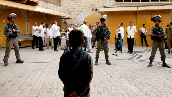 A Palestinian child looks at Israeli soldiers standing guard as settlers stroll through the market in the divided West Bank town of Hebron, on April 13, 2019. (HAZEM BADER / AFP)