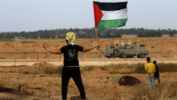 A Palestinian protester wearing a mask waves a national flag during a demonstration near the border with Israel, east of Khan Yunis in the southern Gaza Strip, on April 26, 2019.  (Said KHATIB / AFP)