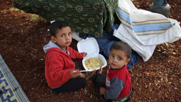 Displaced Syrian children eat in a field near a camp for displaced people in the village of Atme, in the jihadist-held northern Idlib province on May 8, 2019. (AFP)