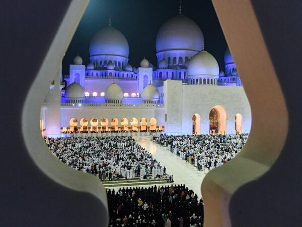 This picture taken early on June 1, 2019 through the crenellations of the Sheikh Zayed Grand Mosque in the UAE capital Abu Dhabi shows Muslim worshippers praying in the mosque's courtyard on the occasion of Lailat al-Qadr, which marks the night in the fasting month of Ramadan during which the Koran was first revealed to Prophet Mohammed in the seventh century.  KARIM SAHIB / AFP