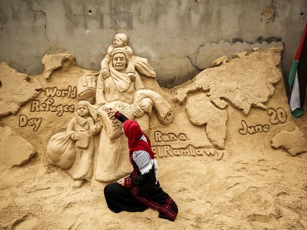 Palestinian sand sculptor Rana Ramlawi finishes a new artwork creation commemorating World Refugee Day, a day dedicated by the United Nations General Assembly to raising awareness of the situation of refugees throughout the world, in Gaza City on June 20, 2020, depicting a woman carrying a child and a sack of flour bearing the logo of the United Nations Relief and Works Agency for Palestine Refugees (UNRWA). MOHAMMED ABED / AFP