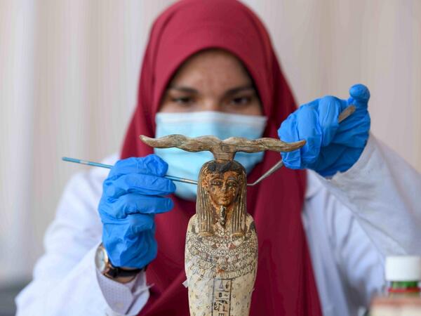 An archaeologist cleans a statue during the unveiling of an ancient treasure trove of more than a 100 intact sarcophagi, at the Saqqara necropolis 30 kms south of the Egyptian capital Cairo, on November 14, 2020. Egypt announced the discovery of an ancient treasure trove of more than a 100 intact sarcophagi, the largest such find this year. The sealed wooden coffins, unveiled on site amid fanfare, belonged to top officials of the Late Period and the Ptolemaic period of ancient Egypt. They were found in thre