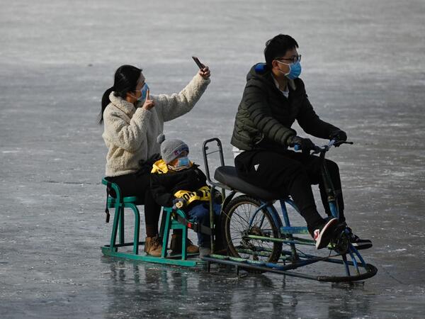 A family use mobile phone to take a selfie as they ride sled on a frozen lake in Beijing on January 12, 2021. WANG Zhao / AFP