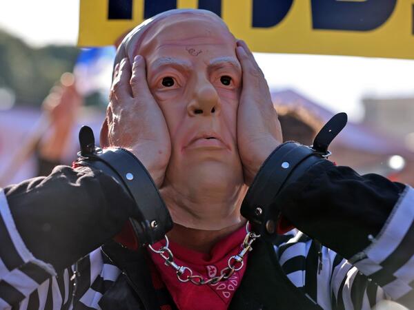 A demonstrator wearing a mask representing Prime Minister Benjamin Netanyahu gestures during a demonstration outside the court, as his corruption trial resumes in occupied east Jerusalem, on February 8, 2021. Israel's Prime Minister Benjamin Netanyahu returns to court to formally respond to the corruption charges against him, as his trial enters an intensified phase six weeks before he faces re-election. EMMANUEL DUNAND / AFP