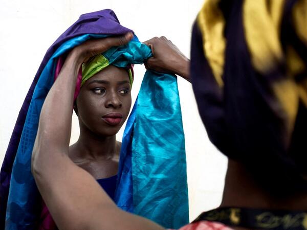 A dresser helps a gold miner to wear a turban in the backstage prior to take part in a fashion show as part of the first edition of the International Gold Fair Afrik'Or, in Bamako, on February 12, 2021. The Princess of Burundi Esther Kamatari, selected 34 women among gold mines workers in southern Mali, to walk down the catwalk for a fashion show organised during the International Gold Fair. Gold represents 15% of Mali's exports and more than 20% of its GDP estimated at nearly US$20 billion by the end of 20