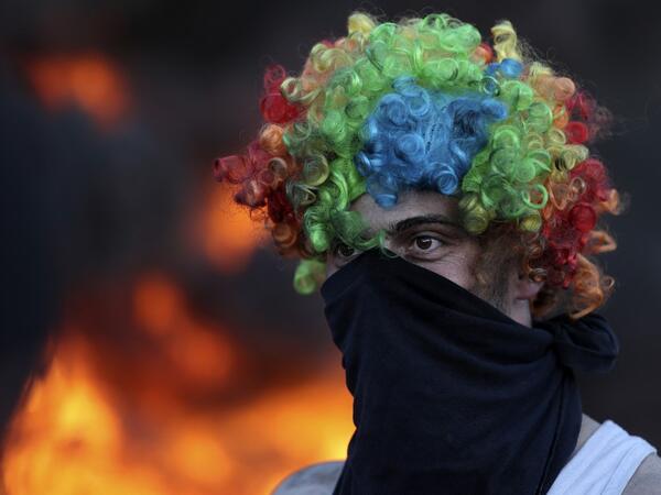 A man wears a face cover and a colorful wig as Palestinians burn tires during a night demonstration the expansion of the Jewish settlement outpost of Eviatar on the lands of Beita village, near the occupied West Bank city of Nablus, 