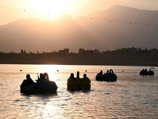 In this photograph taken on September 28, 2021 Taliban fighters ride on paddle boats at Qargha Lake on the outskirts of Kabul. "This is Afghanistan!" a Taliban fighter shouts on the pirate ship ride at a fairground in western Kabul, as his armed comrades cackle and whoop on board the rickety attraction. (Photo by WAKIL KOHSAR / AFP) / TO GO WITH: AFGHANISTAN-CONFLICT-FAIRGROUND, SCENE BY JAMES EDGAR - TO GO WITH: Afghanistan-conflict-fairground, SCENE by James EDGAR