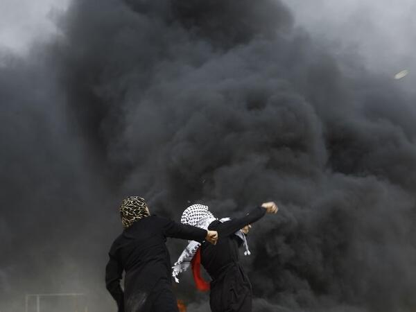 Palestinian women attend throw stones past smoke plume rusing from burning tires during clashes with Israeli forces across the border, following a demonstration calling for the right to return -- meaning Palestinian refugees being allowed to go back to the land they fled or were expelled from during the 1948 war surrounding Israel's creation -- near the border with Israel, east of Gaza City, in the southern Gaza Strip, on Apr. 20, 2018. 
(MOHAMMED ABED / AFP)