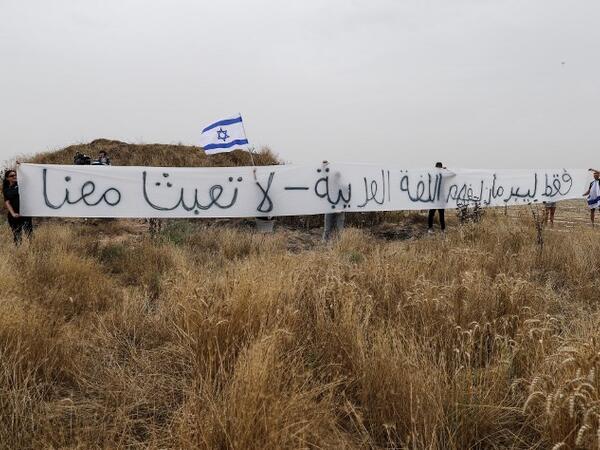 A picture taken on May 4, 2018 from the southern Israeli kibbutz of Nahal Oz across the border with the Gaza Strip shows Israeli settlers waving an Israeli flag and holding a banner reading in broken Arabic "Only Lieberman understands the Arabic language -- do not mess with us", during clashes between Israeli forces and Palestinian protesters on the sixth straight Friday of mass demonstrations calling for the right of Palestinians to return to their historic homelands. (AHMAD GHARABLI / AFP)