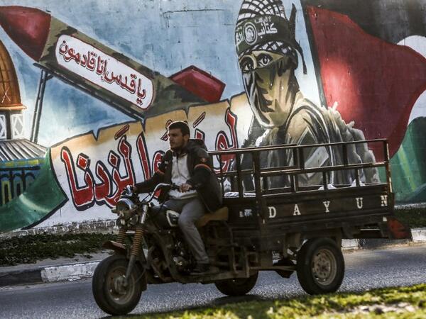 A Palestinian drives a motorcycle cart past a mural depicting a masked fighter of the Qassam Brigades, the armed wing of the Hamas movement, next to a missile with a caption reading in Arabic "Oh Jerusalem, we are coming" and the Dome of the Rock, in a street in Rafah in the southern Gaza Strip 
SAID KHATIB / AFP