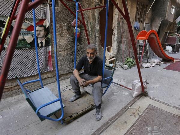 A man sits on a swing next to images of the late Palestinian leader Yasser Arafat and the Syrian President Bashar al-Assad in Yarmuk camp southern Damascus on November 1, 2018. 
LOUAI BESHARA / AFP