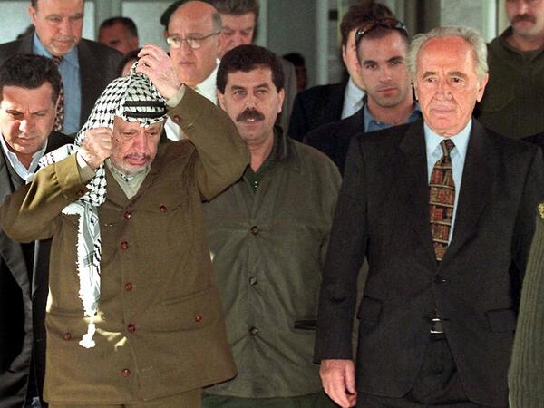 This file photo taken on February 11, 1999 shows Palestinian leader Yasser Arafat (L) adjusting his kaffiyeh, as he walks with former Israeli Prime Minister Shimon Peres to a press conference in Gaza City. (AFP/Fayez Nureldine)